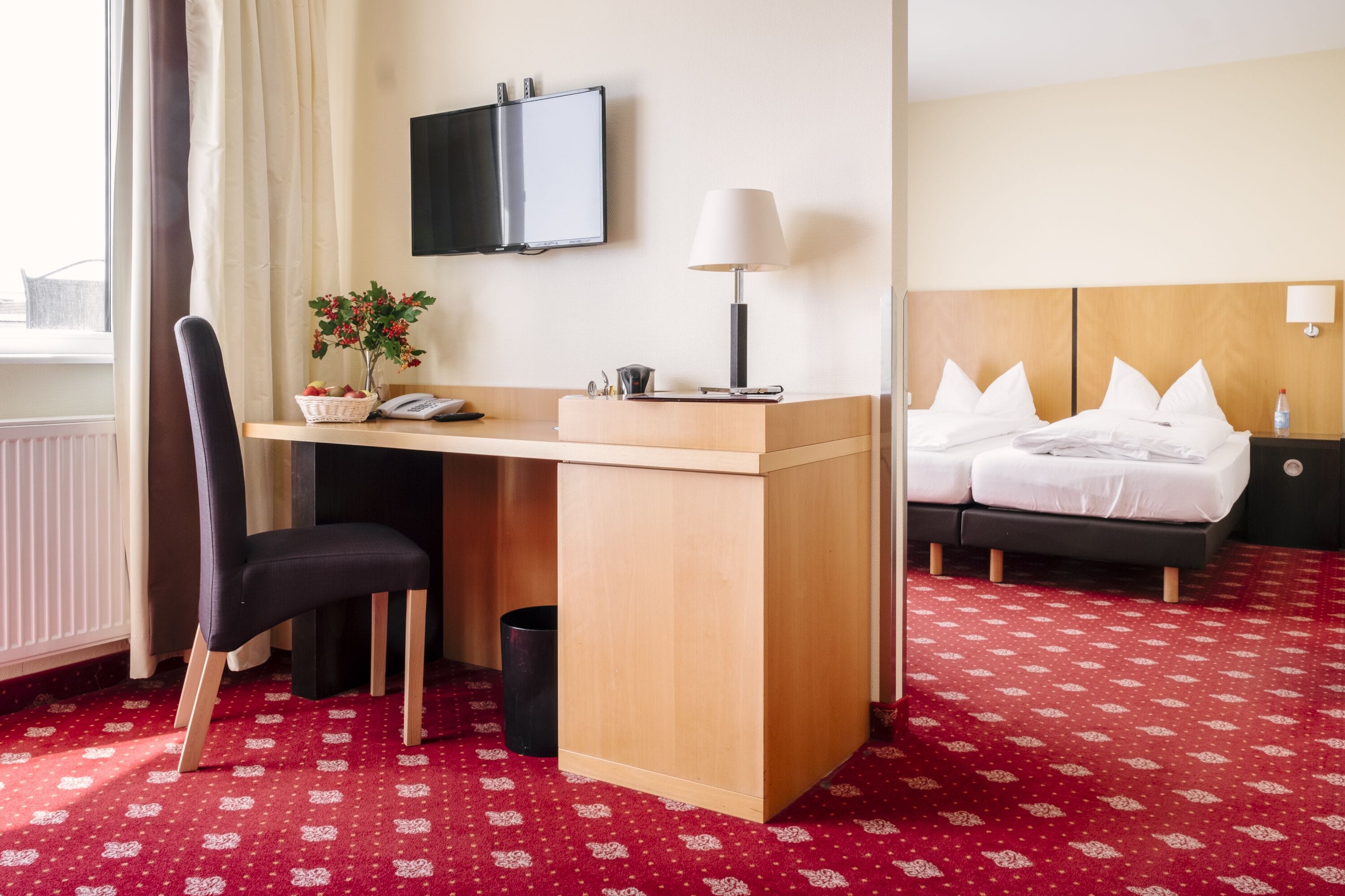 A hotel room with a desk, chair, bed, and a TV mounted on the wall.