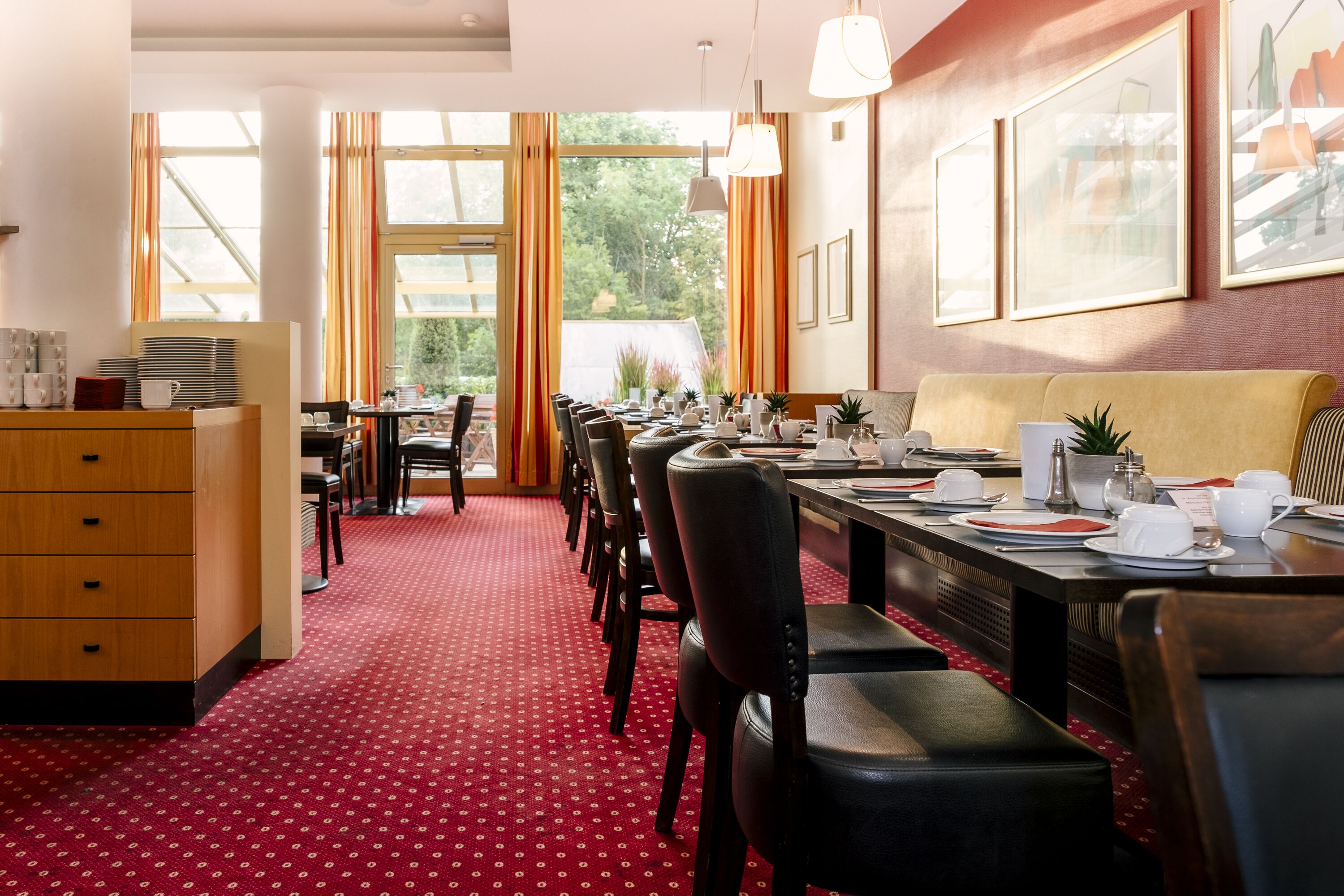Comedor con una mesa larga dispuesta para varios invitados, sillas, un sofá y un mueble con objetos apilados.