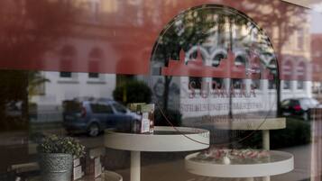 A hotel window with a circular logo and text, a small table with a potted plant, and a reflection of a building and parked car.