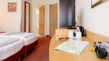 A hotel room with a bed, a desk with a camera, a map, and a mirror.