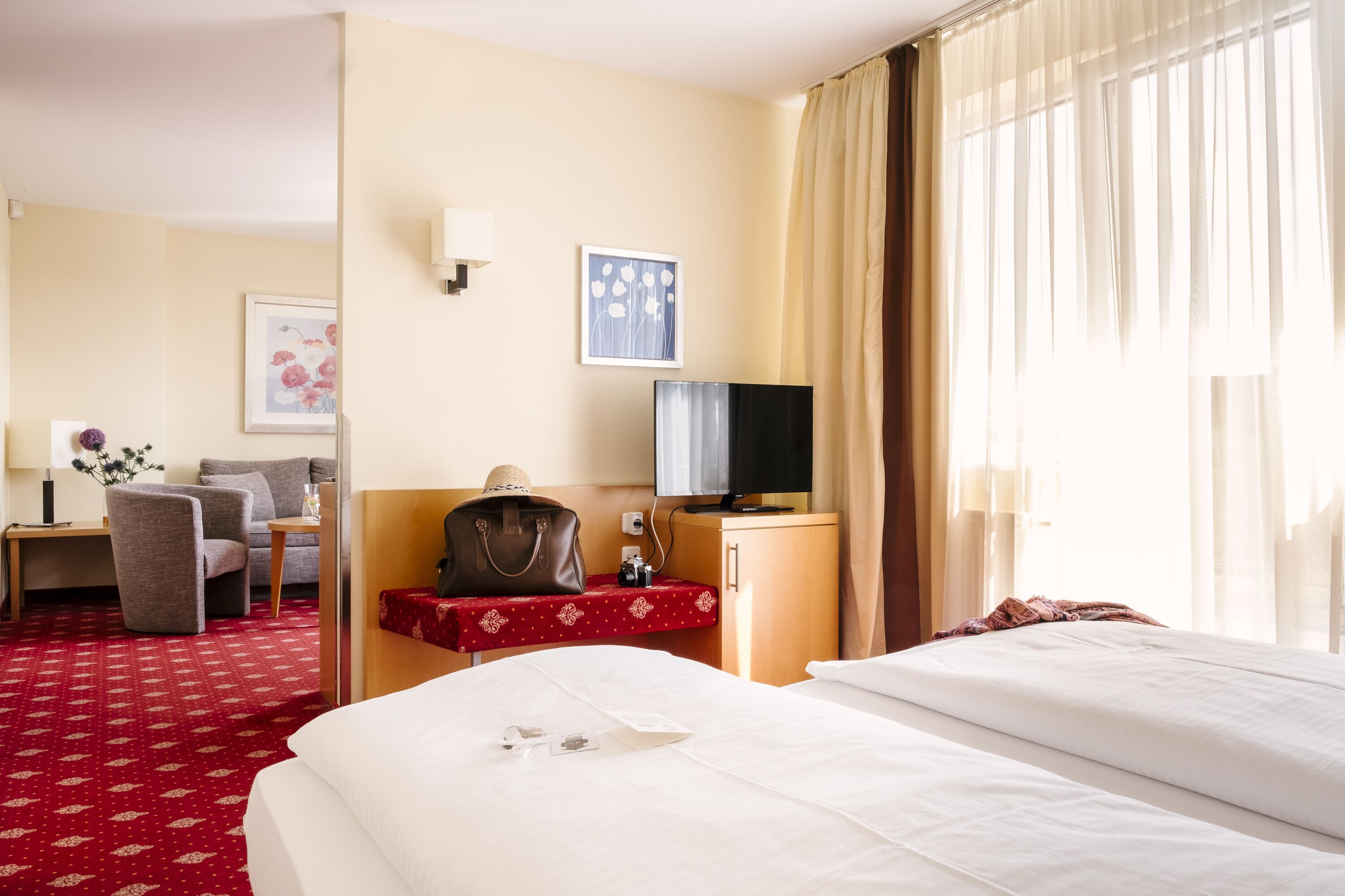 Une chambre d’hôtel avec un lit, un bureau et une chaise, une télévision et une fenêtre avec des rideaux.