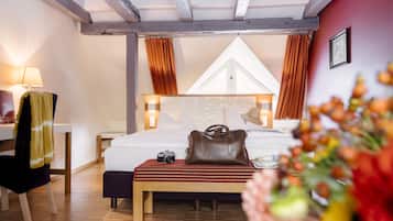 A hotel room with a bed, a desk, a chair, a lamp, a handbag, and a bench.