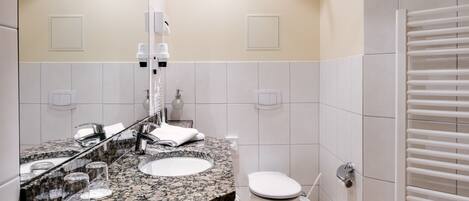 Un baño con lavamanos de encimera de granito, inodoro blanco y perchero para toallas.