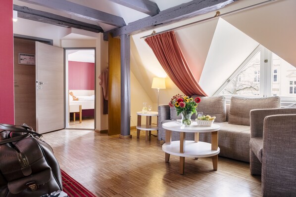 Una habitación de hotel moderna con suelo de madera, un sofá, una mesa de centro con un florero y vistas a través de un ventanal grande.