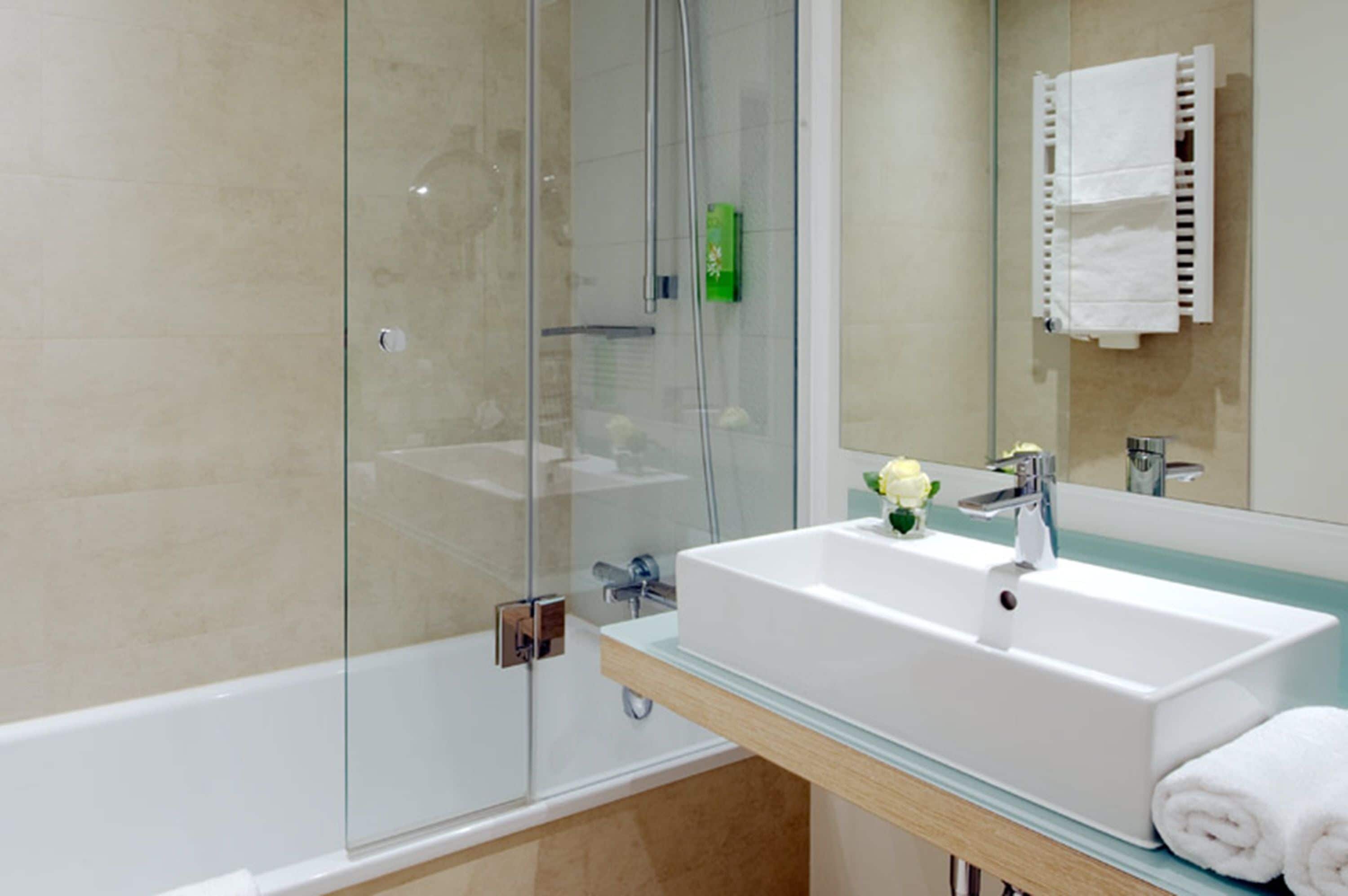 A modern bathroom with a glass-enclosed shower, a white sink, and a mirror above it.
