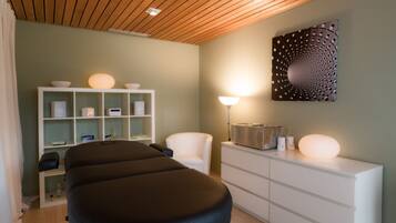 Relax in a serene space with a central massage table, shelving unit, and modern dresser.