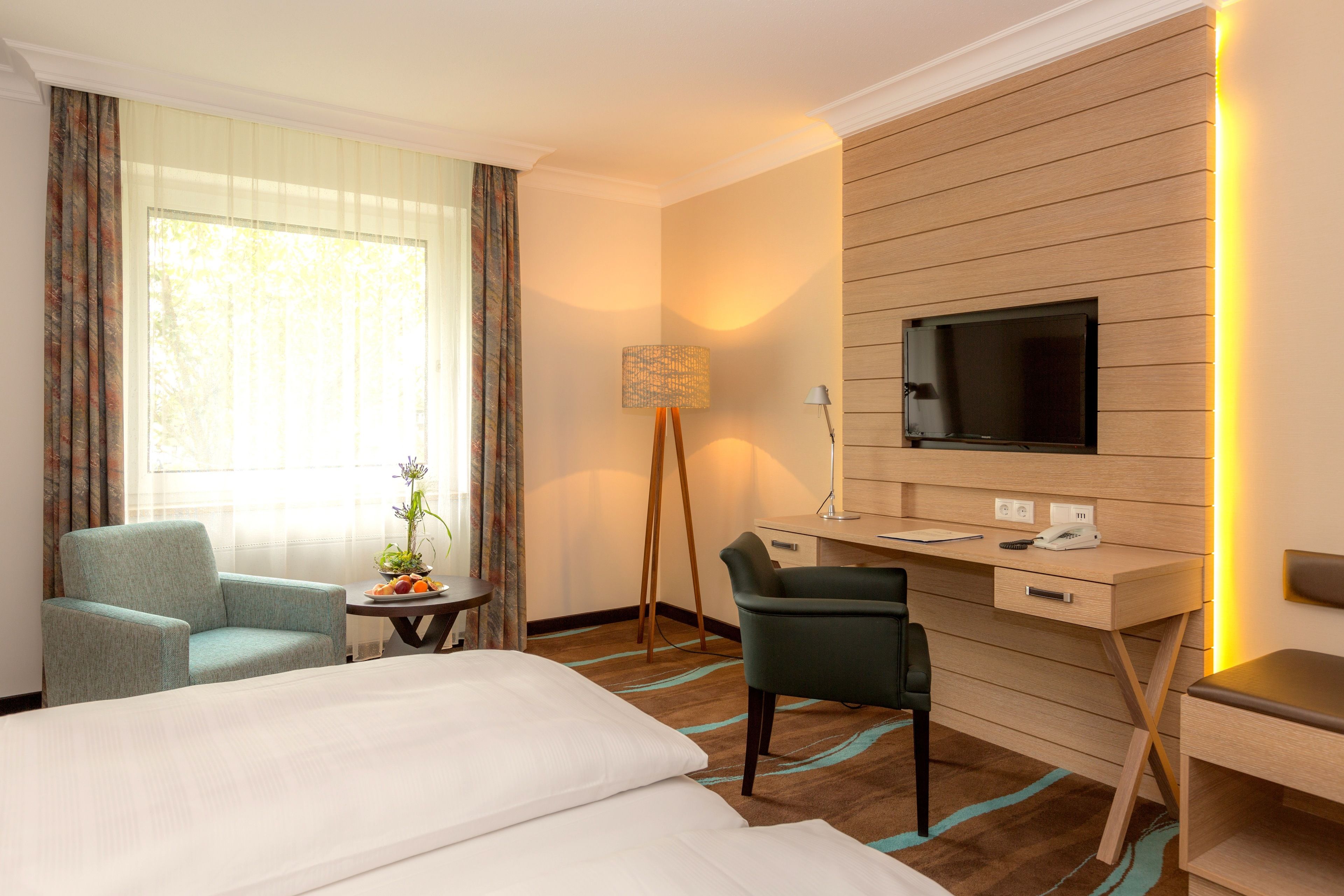A hotel room with a bed, a desk, a chair, a TV, and a lamp.