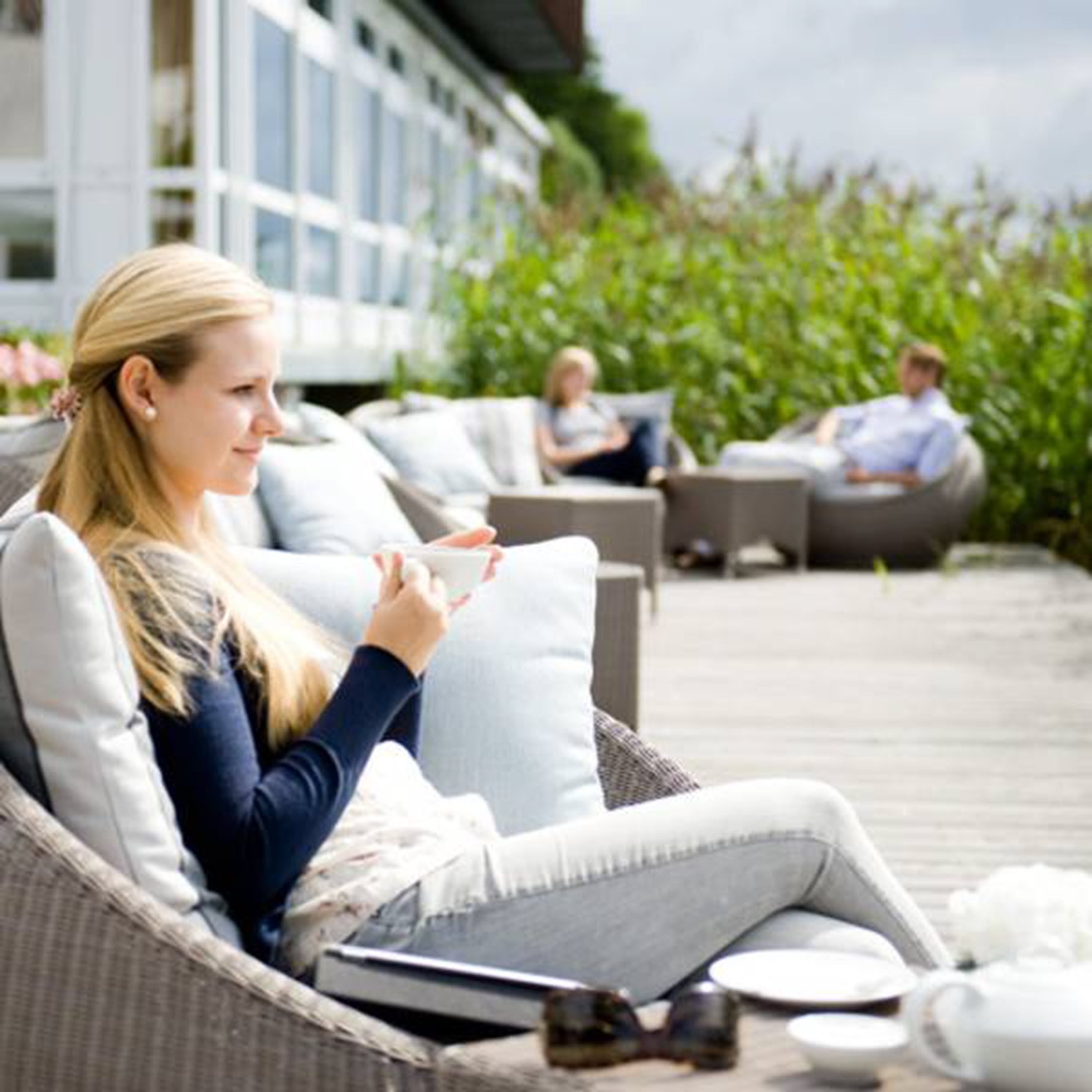 Een moderne zithoek buiten met rieten meubels en een houten terras.