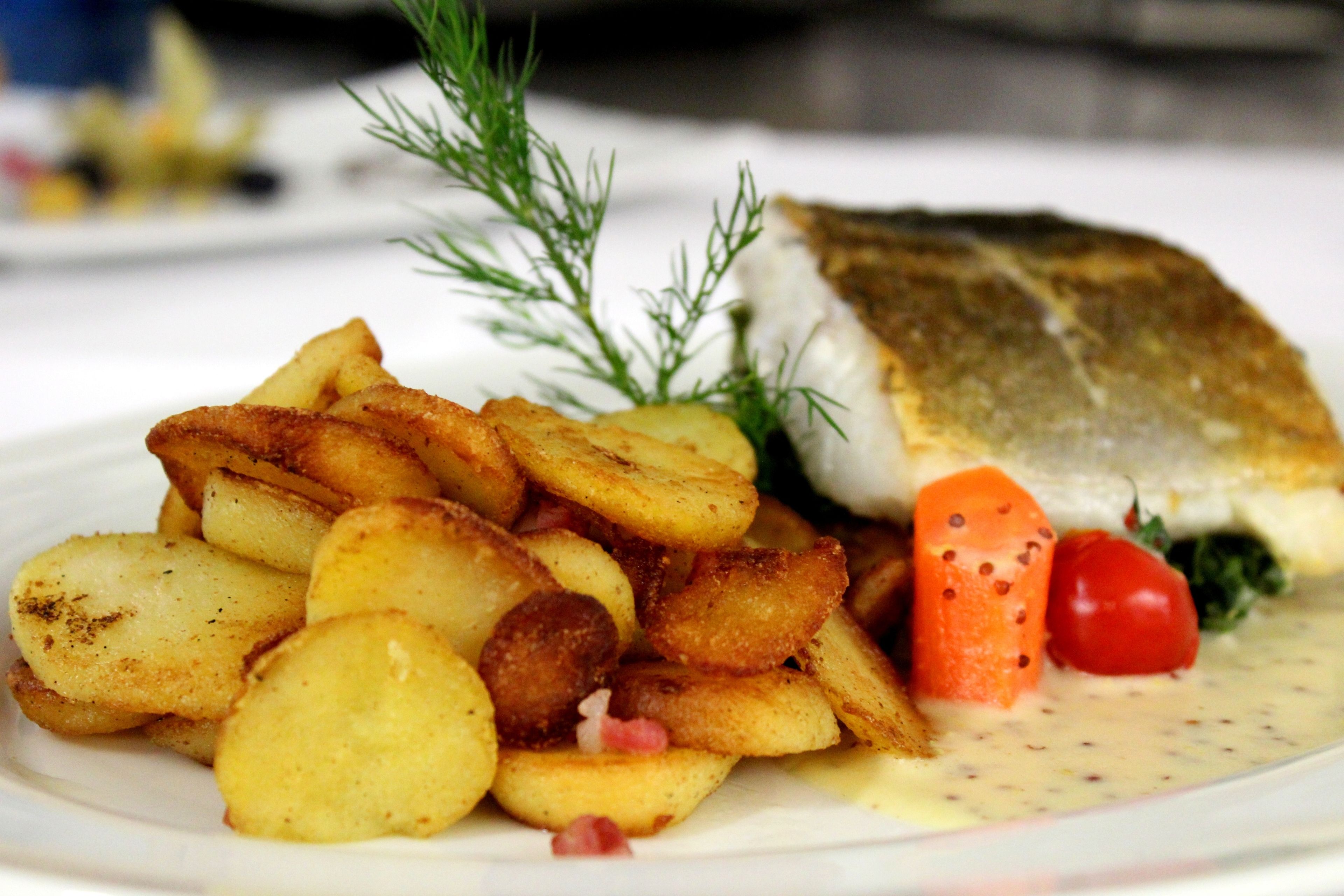 Ein Teller mit Fischfilet, Bratkartoffeln und einer Garnitur aus Dill und Kirschtomaten.