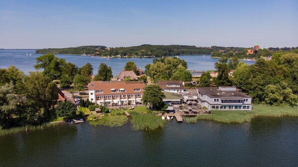 A lakeside property with multiple buildings, including a large house with a red roof and a modern building with large windows.