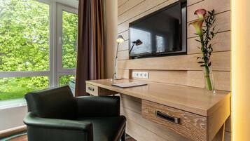 A modern room with a wooden desk, a chair, a flat-screen TV mounted on the wall, a desk lamp, and a vase with a plant.