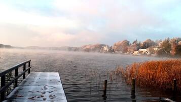 A wooden pier extending into a misty lake with a row of houses in the background.