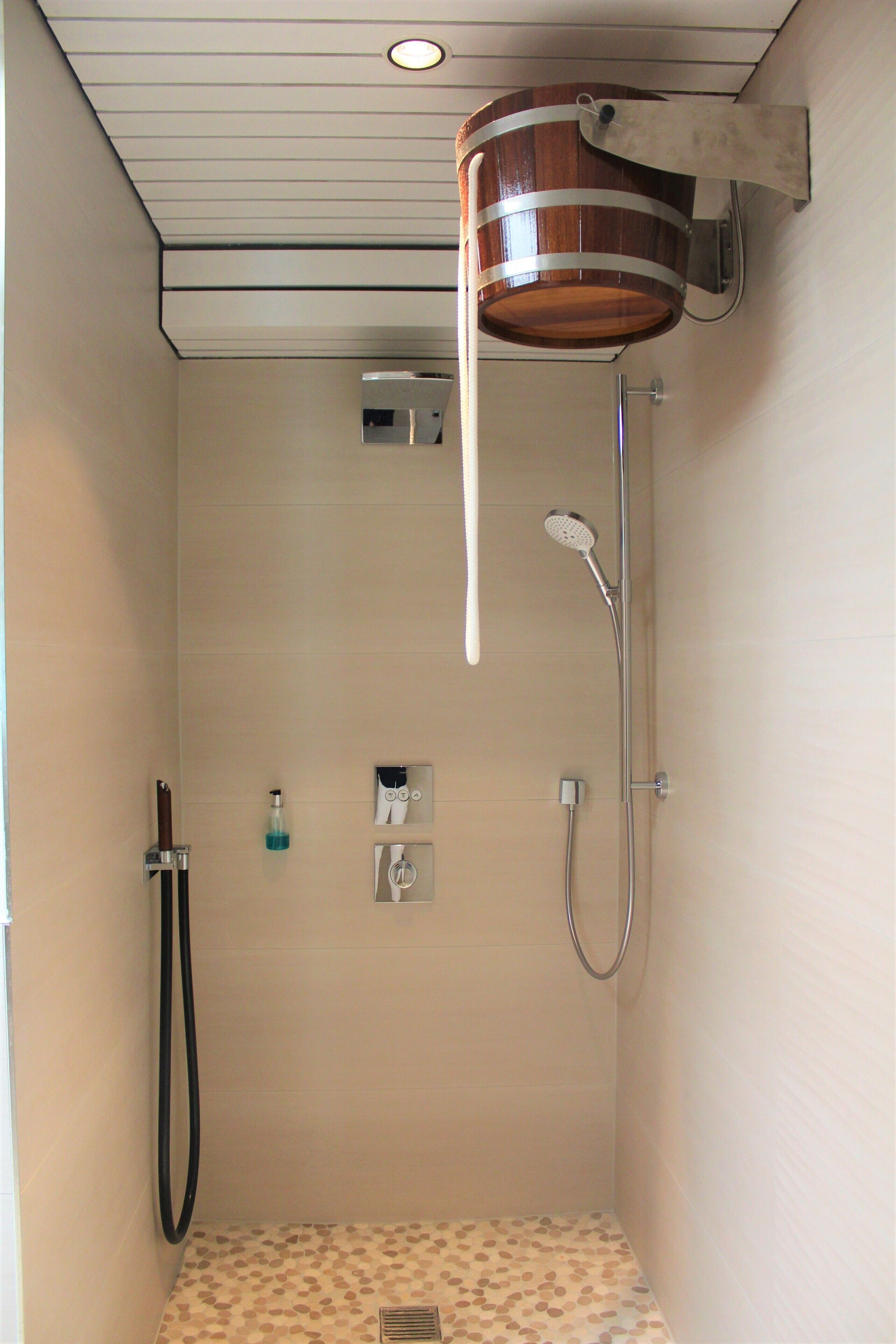 A shower with a wooden bucket, a handheld showerhead, and a handheld hose.
