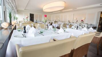 Een elegante eetzaal met witte tafellnen, keurig gedekte tafels en beige stoelen.