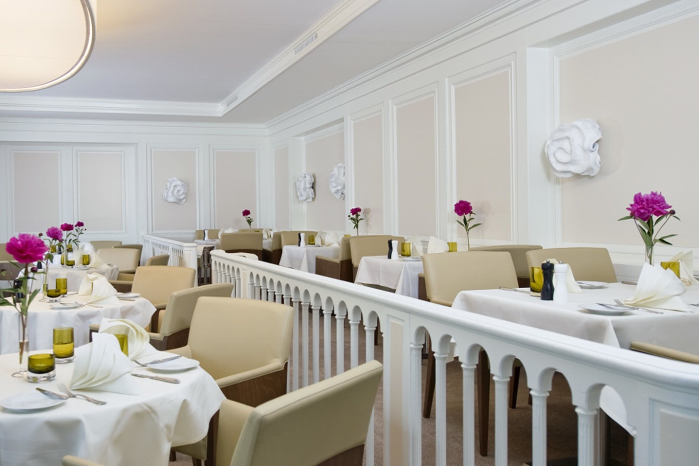 A formal dining area with white tables, beige chairs, and pink flowers.