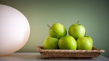 A wicker basket containing five green apples on a table against a green wall.