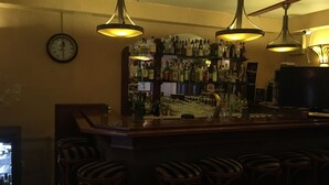 A bar area with a wooden counter, multiple hanging pendant lights, and a clock on the wall. - Hotel De Weyman (Santpoort-Noord)