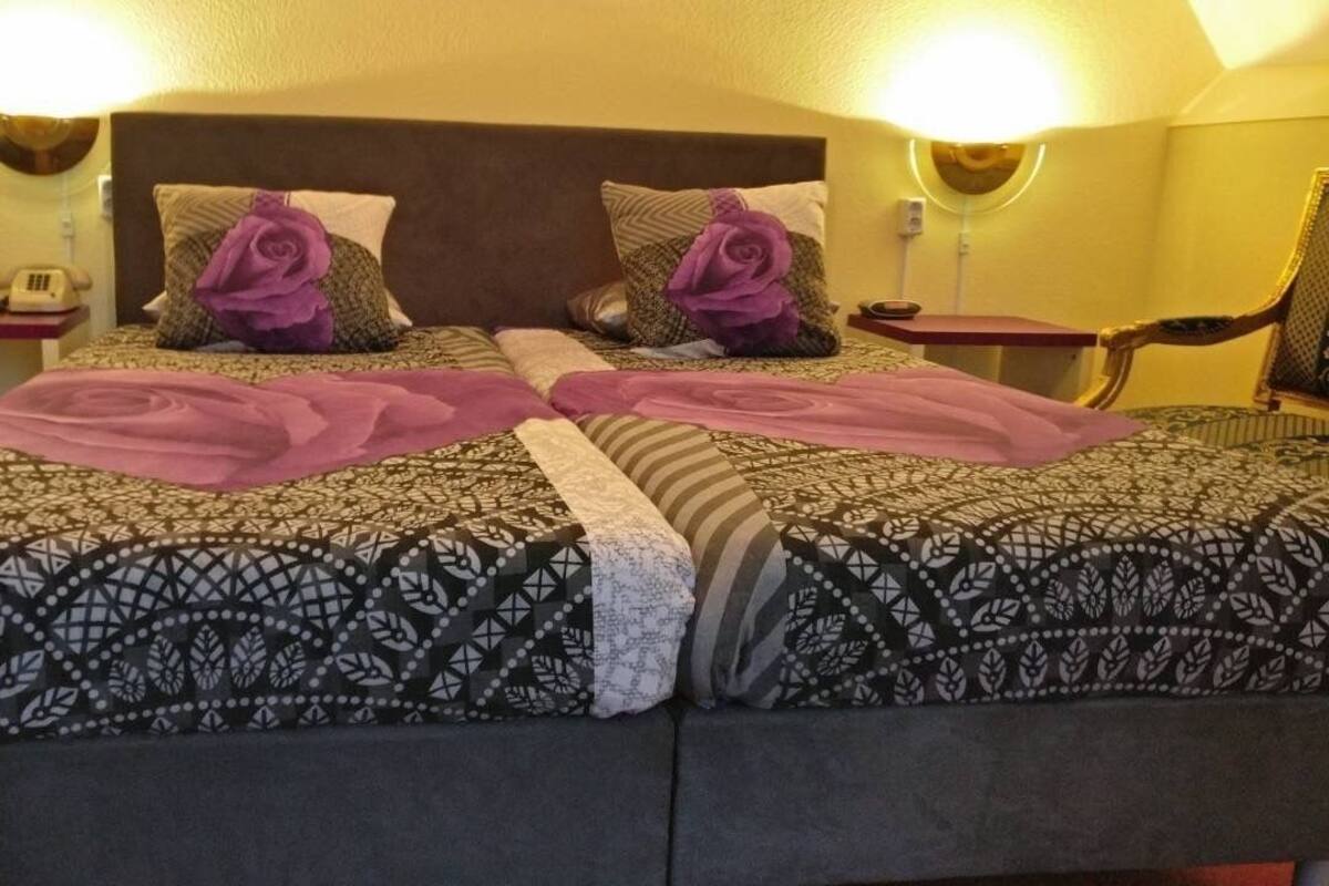 Un lit double avec une literie à motifs et des coussins décoratifs, une table de chevet avec une lampe et une chaise.