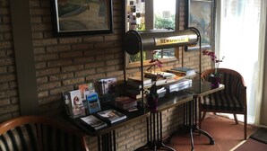 A reception desk with books, a newspaper stand, and a mirror reflecting a brick wall and window. - Hotel De Weyman (Santpoort-Noord)