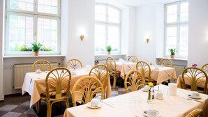 A dining area with multiple tables and chairs, large windows with plants, and a clean, white interior.