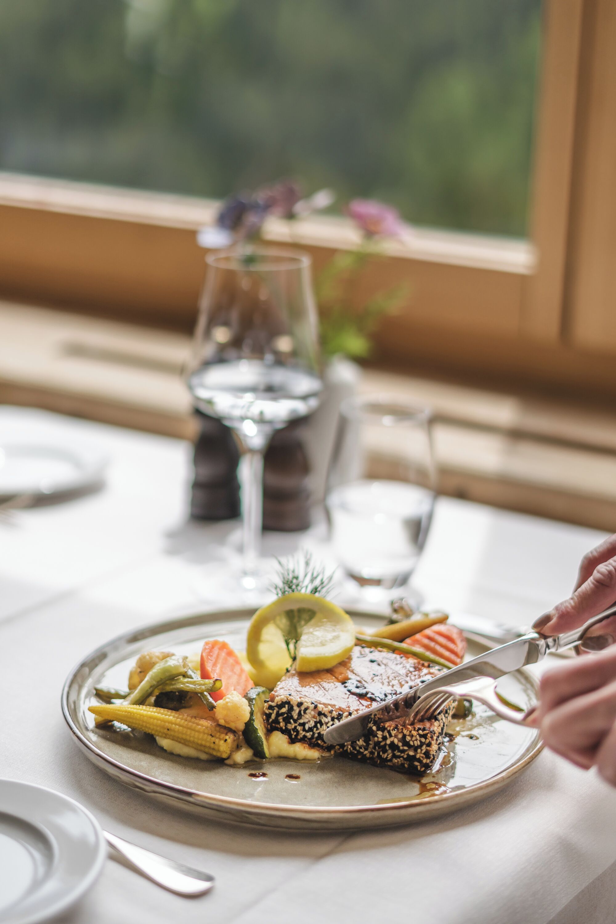 A dining table with a plate of food, a glass of water, and a window view.