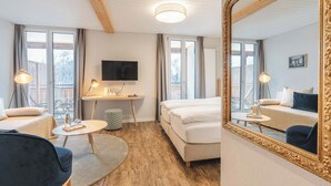 Habitación de hotel con techo de madera, un espejo grande, cama, escritorio con televisor y vistas al exterior.