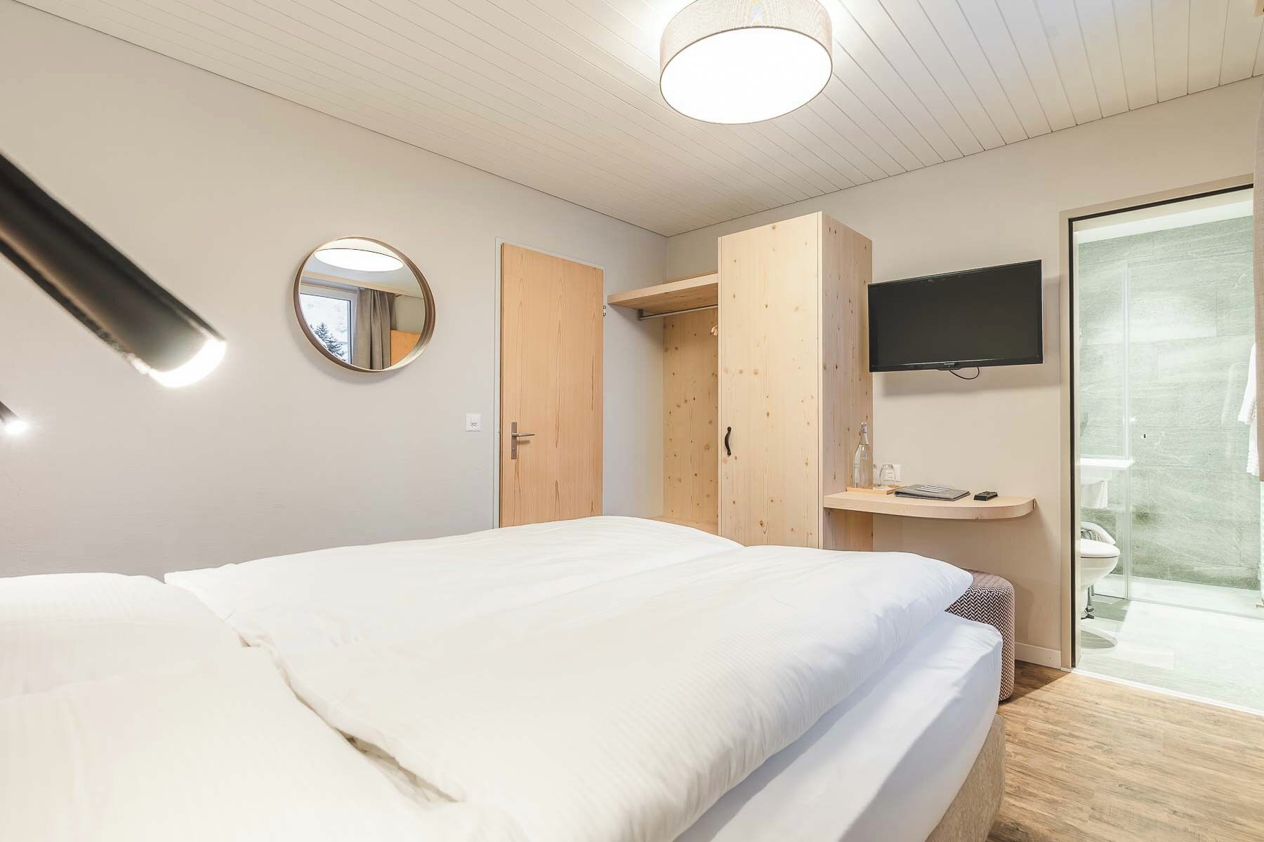 Un dormitorio con cama, televisor, espejo y armario.