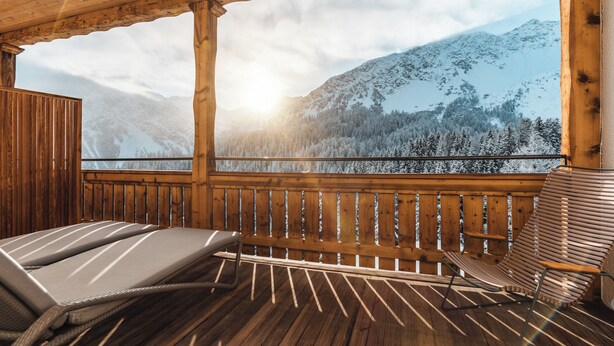 Una terraza de madera con dos sillones reclinables y vistas a montañas nevadas.