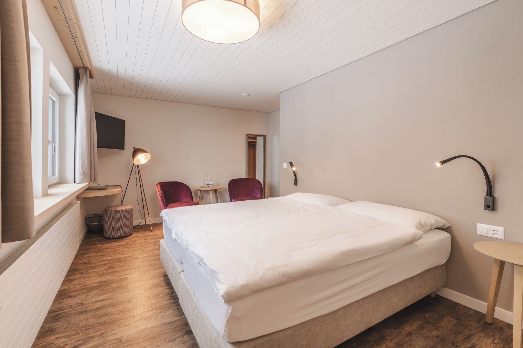 A hotel room with a large bed, a desk, a chair, a TV, and a lamp.