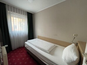 A hotel room with a bed, a radiator, a window with curtains, and a wall socket. - Hotel Hafner (Stuttgart)