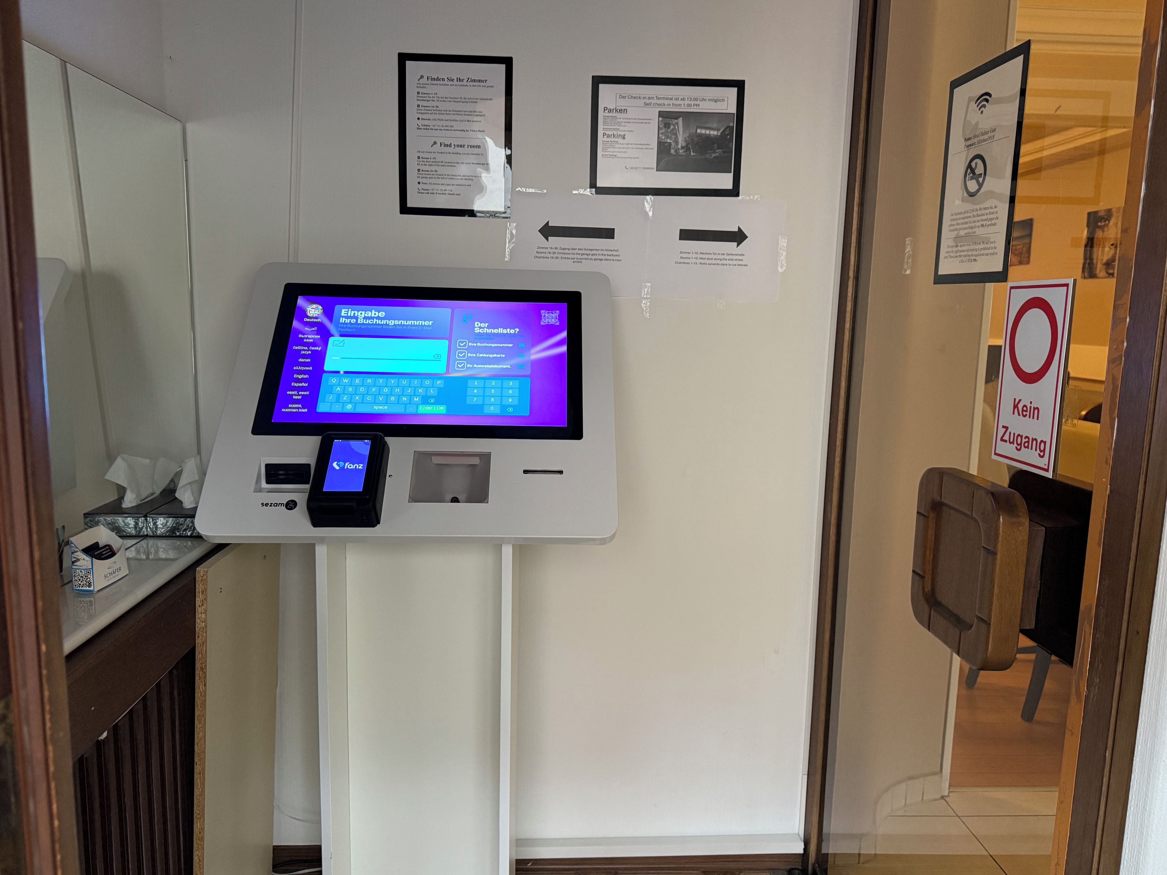 A self-service kiosk with a digital screen, a mobile payment device, and informational posters on the wall.