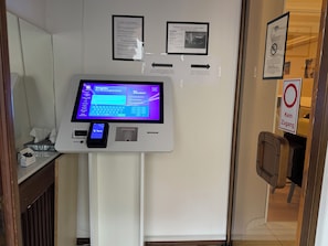 A self-service kiosk with a digital screen, a mobile payment device, and informational posters on the wall. - Hotel Hafner (Stuttgart)