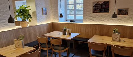 A cozy restaurant interior with wooden tables and chairs, a potted plant, and artwork on the walls.