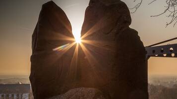 A rock formation with the sun setting behind it, viewed from a wooden platform.