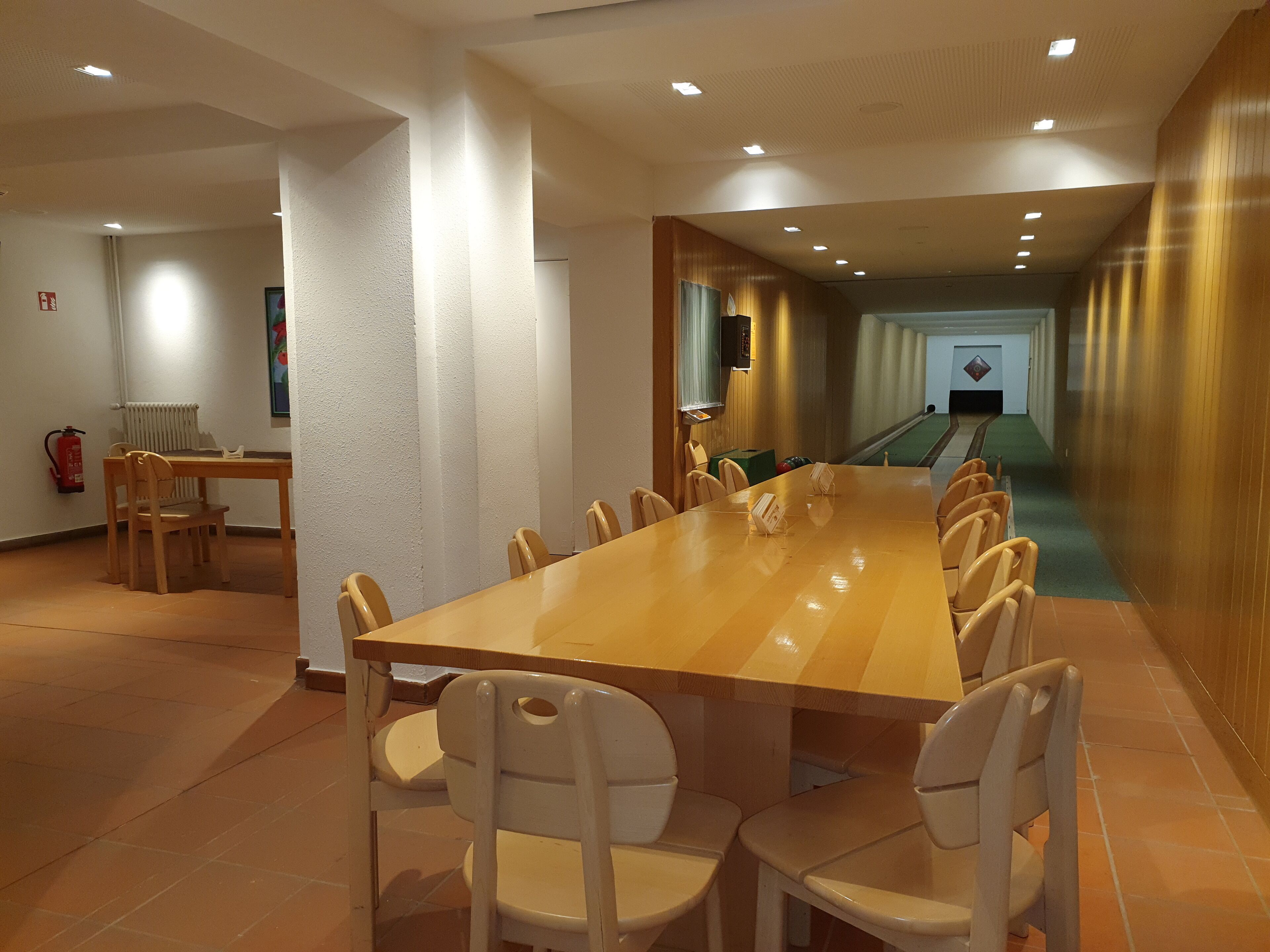 Un salón de conferencias con una larga mesa y sillas, un extintor y una bolera al fondo.