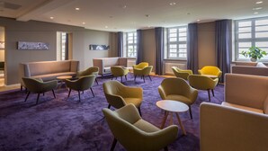 Un hall d’hôtel moderne, doté d’espaces aménagés avec des sièges, de grandes fenêtres et d’œuvres d’art accrochées aux murs.
