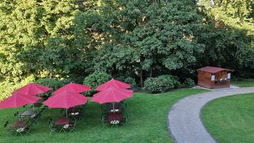 A garden area with outdoor seating under red umbrellas, a wooden structure, and a gravel path.