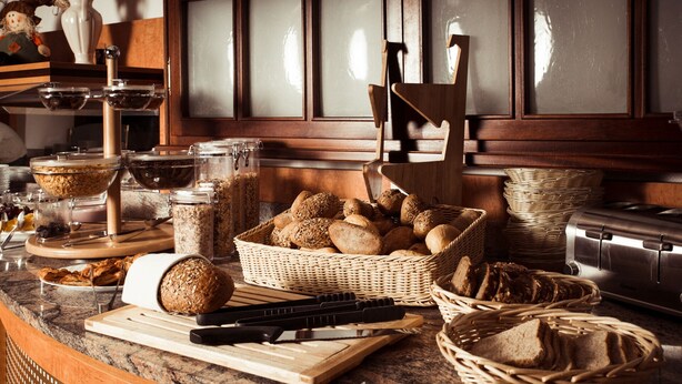 A kitchen counter with various bread and baked goods, a toaster, and a cutting board. - Hotel Astro (Stuttgart)