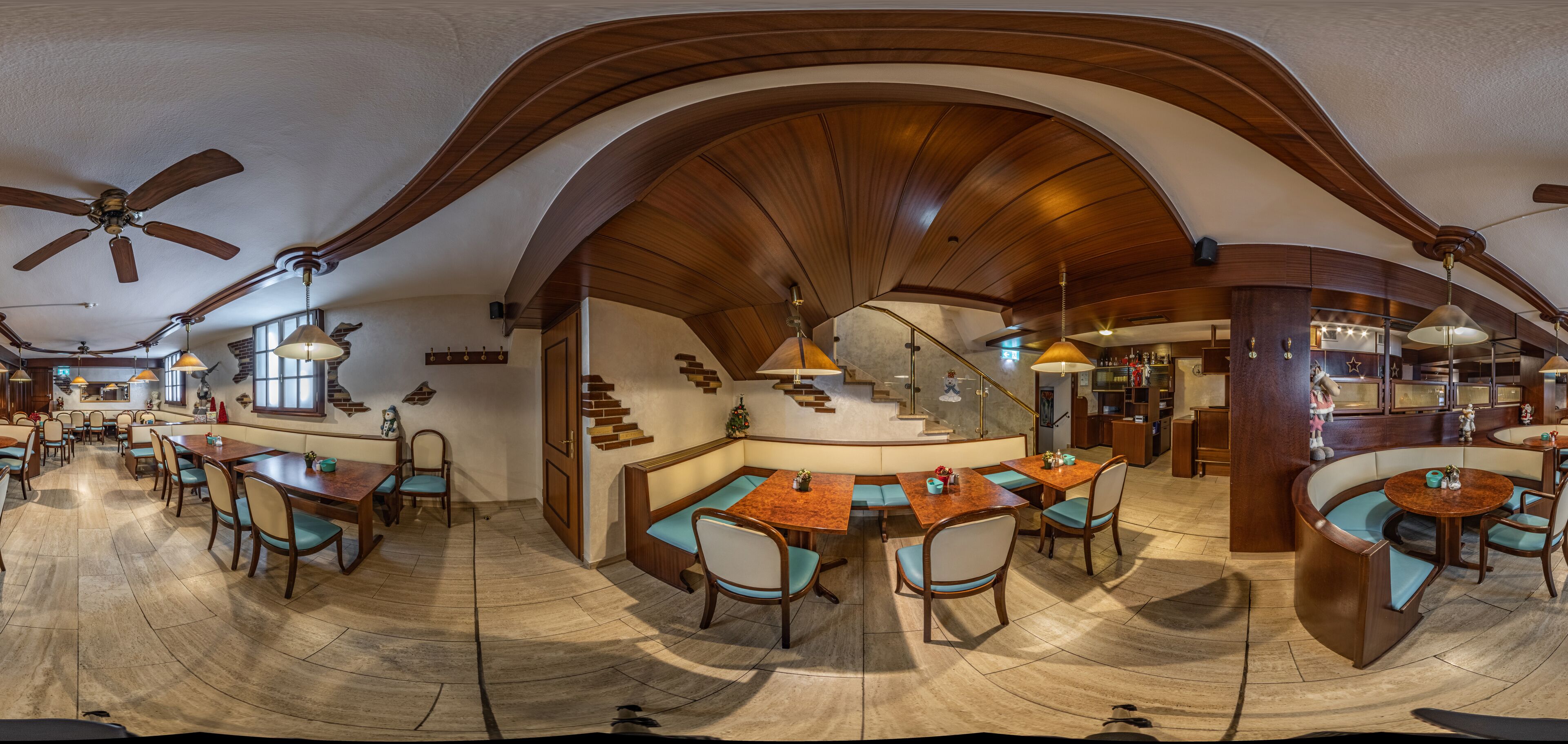 A spacious dining area with wooden tables and chairs, a central seating area, and a staircase leading to an upper level.