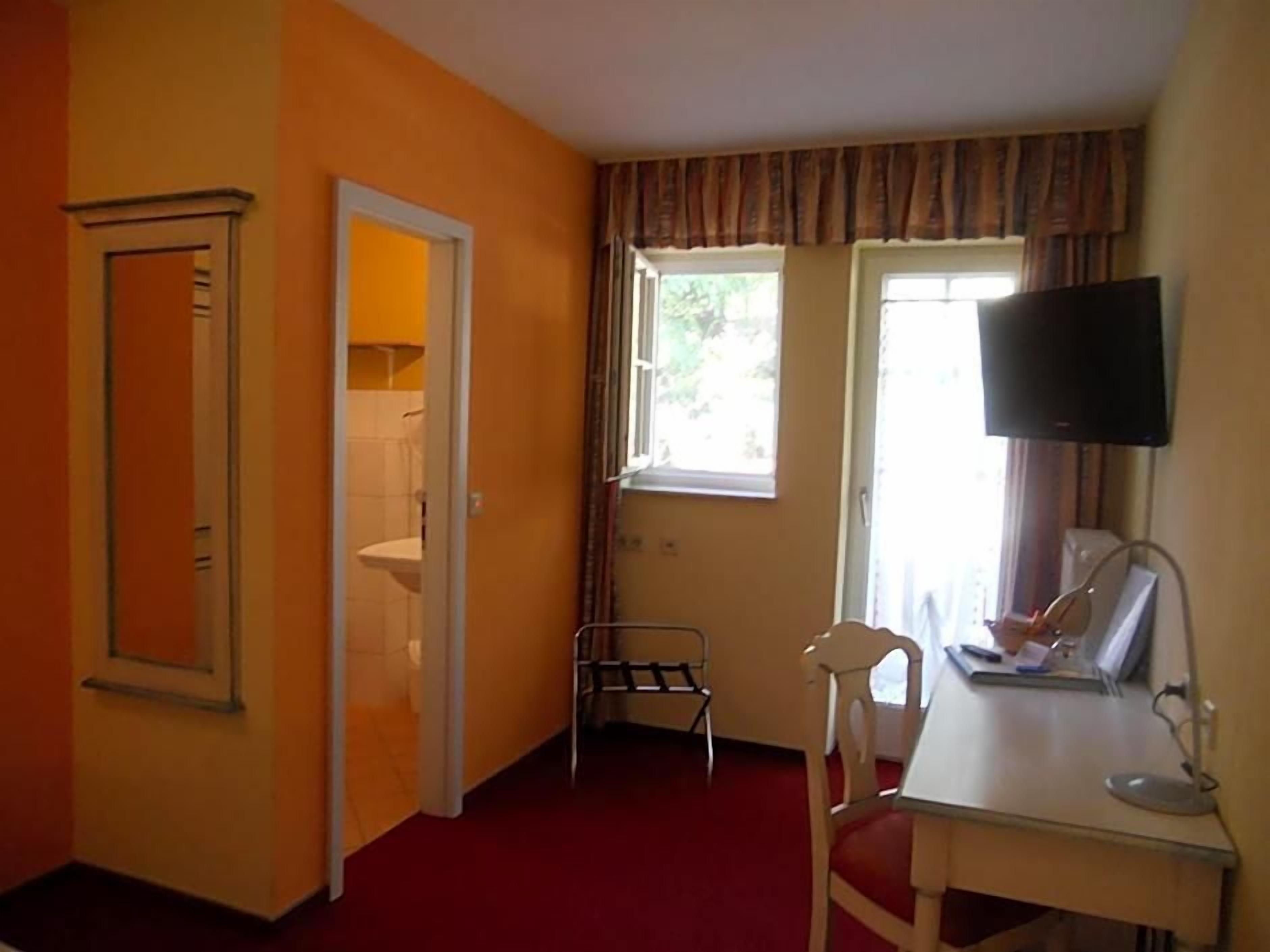 A room with a bed, a desk with a chair, a television, and a window with curtains.
