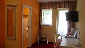 A room with a bed, a desk with a chair, a television, and a window with curtains.