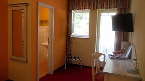 Ein Zimmer mit einem Bett, einem Schreibtisch mit Stuhl, einem Fernseher und einem Fenster mit Vorhängen.