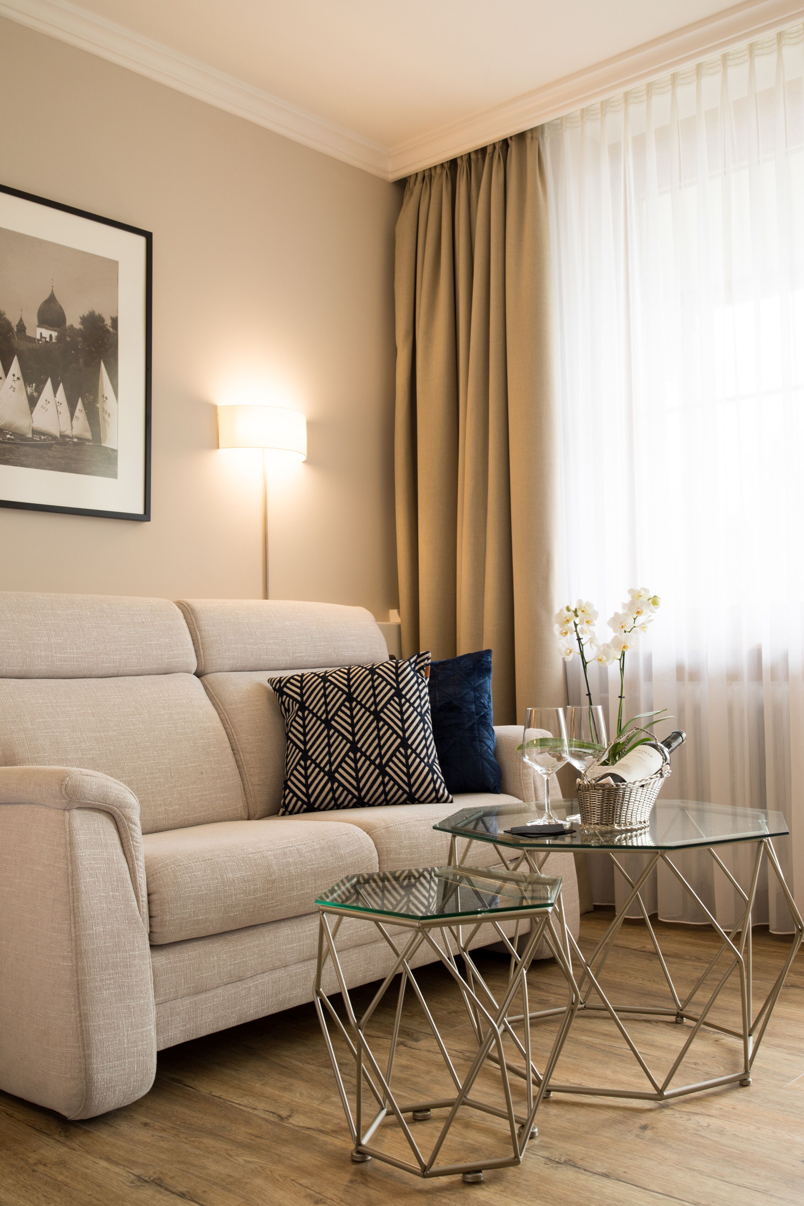 A living room with a sofa, patterned pillows, a glass coffee table, and a framed picture on the wall.