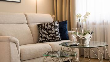 A living room with a sofa, patterned pillows, a glass coffee table, and a framed picture on the wall.