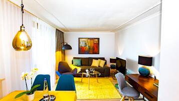 Ein modernes Wohnzimmer mit einem gelben Esstisch, einer Couch und einem Couchtisch. An der Wand hängt ein Gemälde und auf dem Beistelltisch steht eine Lampe.