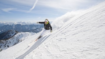 Une personne fait du ski sur une pente enneigée, avec un paysage montagneux en arrière-plan.