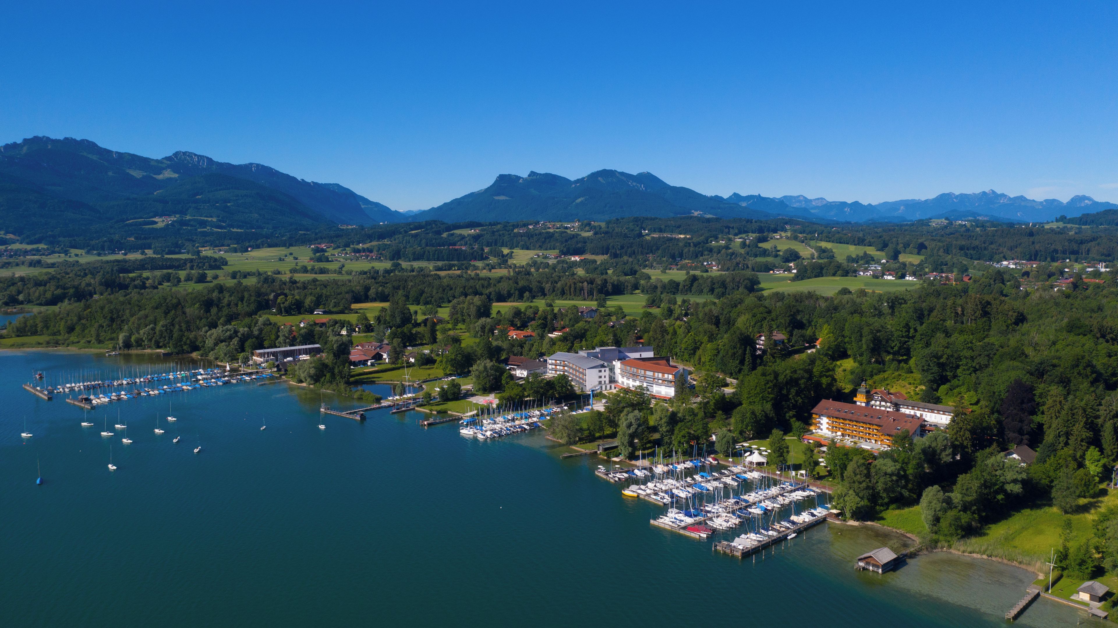 A marina with boats docked, surrounded by lush greenery and mountains in the background.
