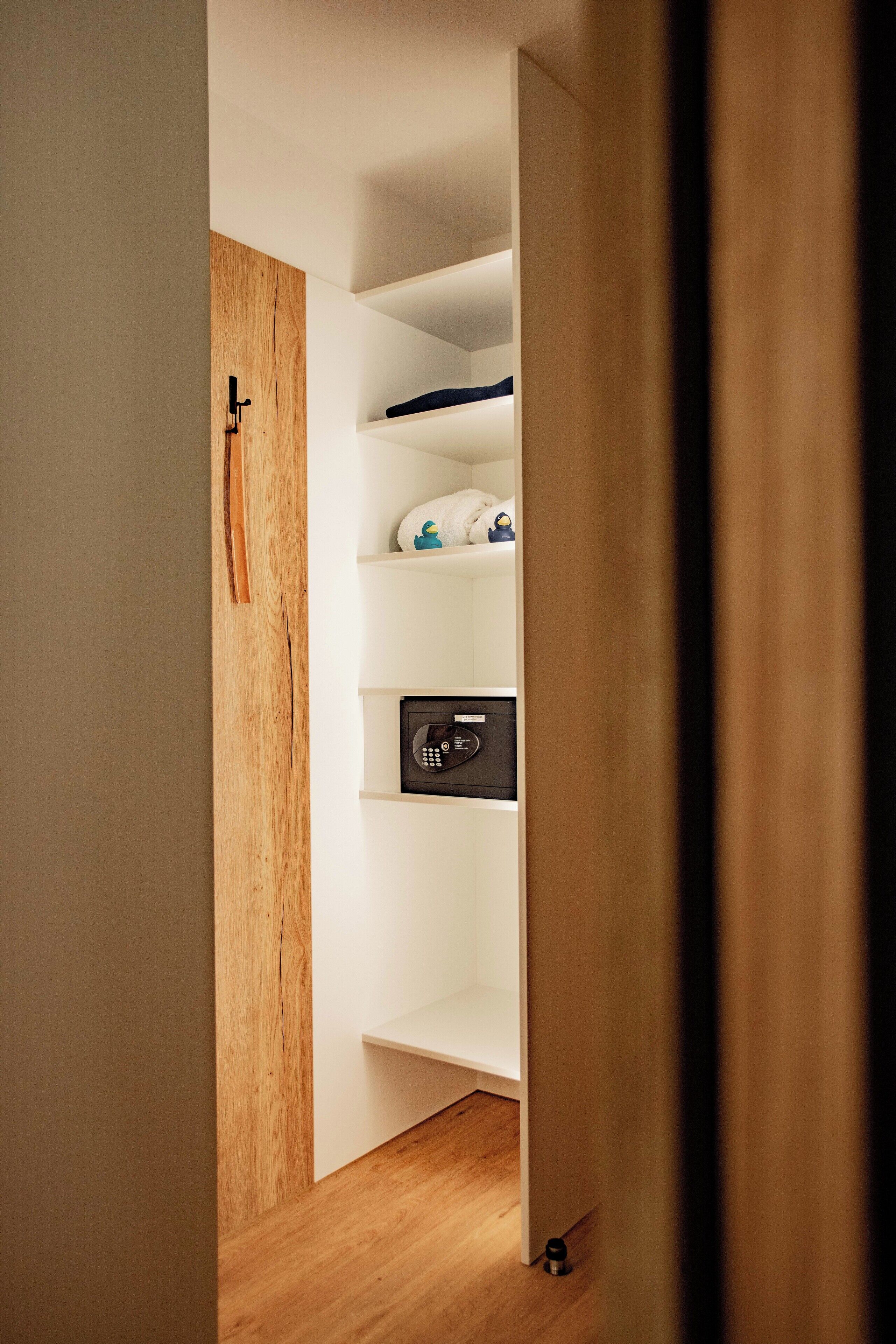 Un estrecho pasillo con suelo de madera y paredes blancas que conduce a una habitación con una estantería empotrada que contiene diversos objetos.