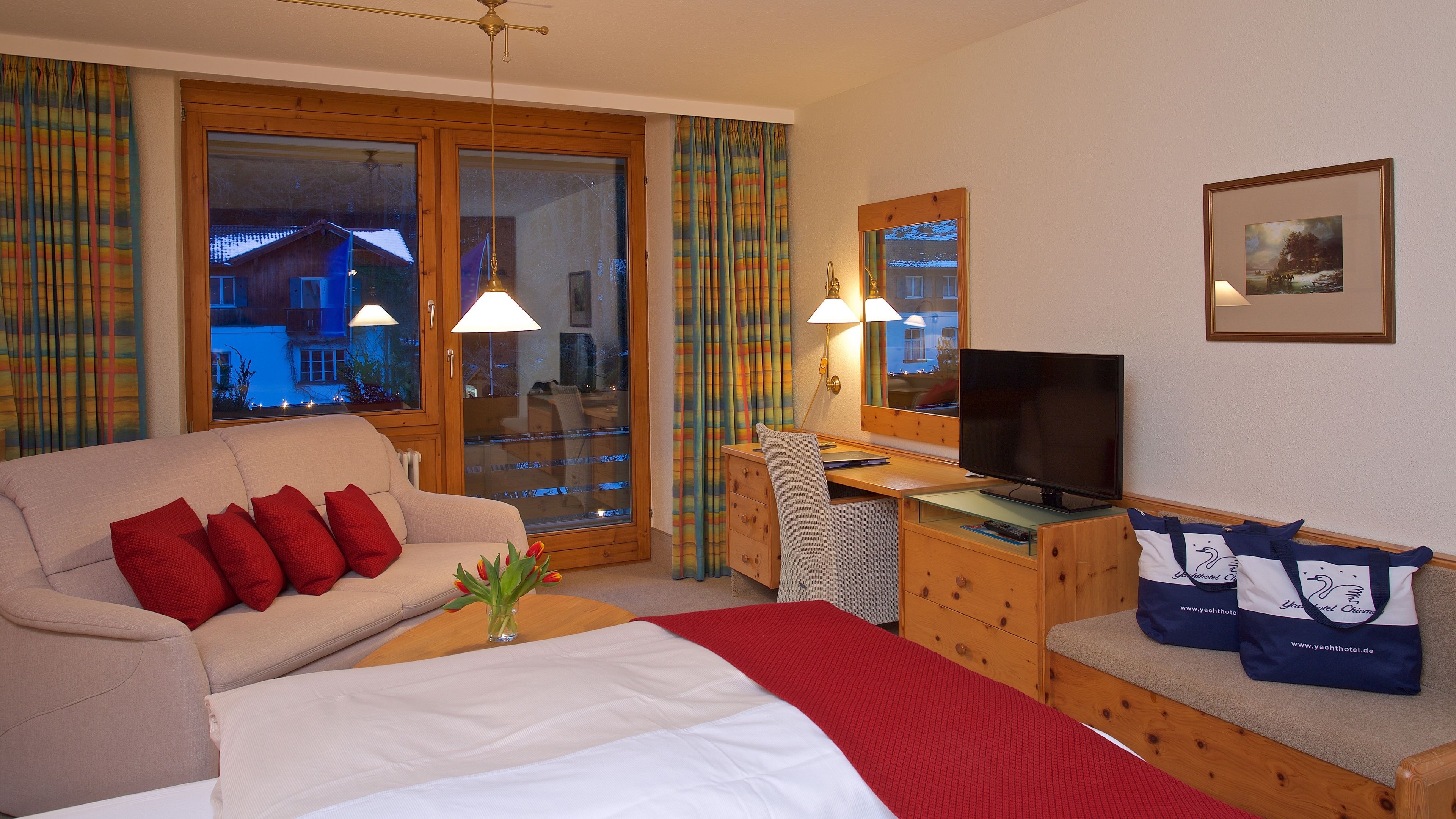 A hotel room with a bed, a sofa, a desk with a TV, and a window with curtains.