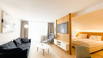 Ein modernes Hotelzimmer mit einer Couch, einem Sessel, einem kleinen Tisch, einem Bett und einem an der Wand befestigten Fernseher.